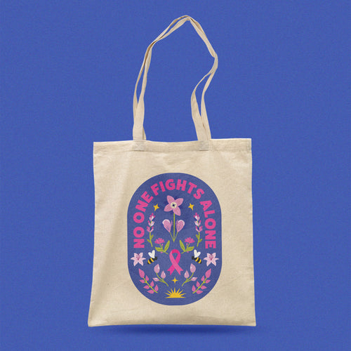 Beige tote bag with a pink ribbon design and 'No One Fights Alone' text affirmation for breast cancer patient