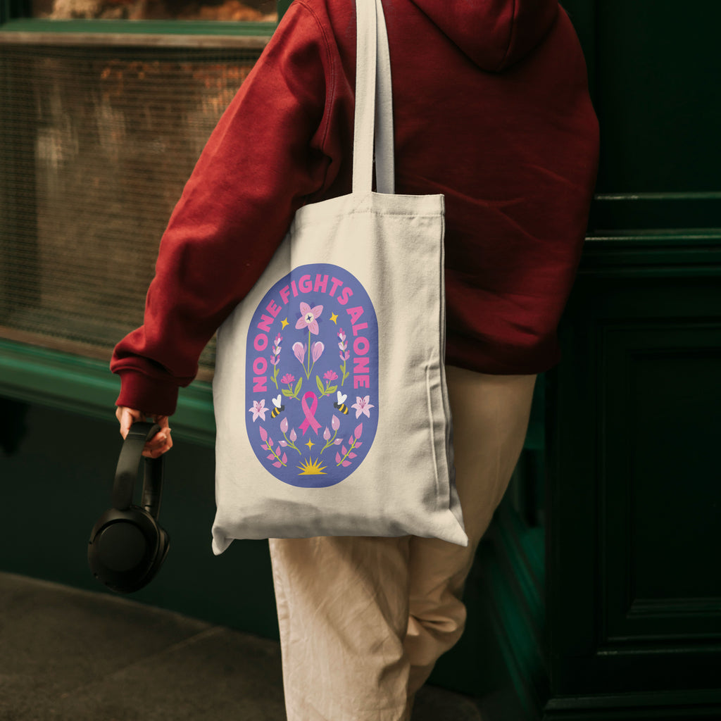 Person wearing a red hoodie holding a tote bag with a pink ribbon design.