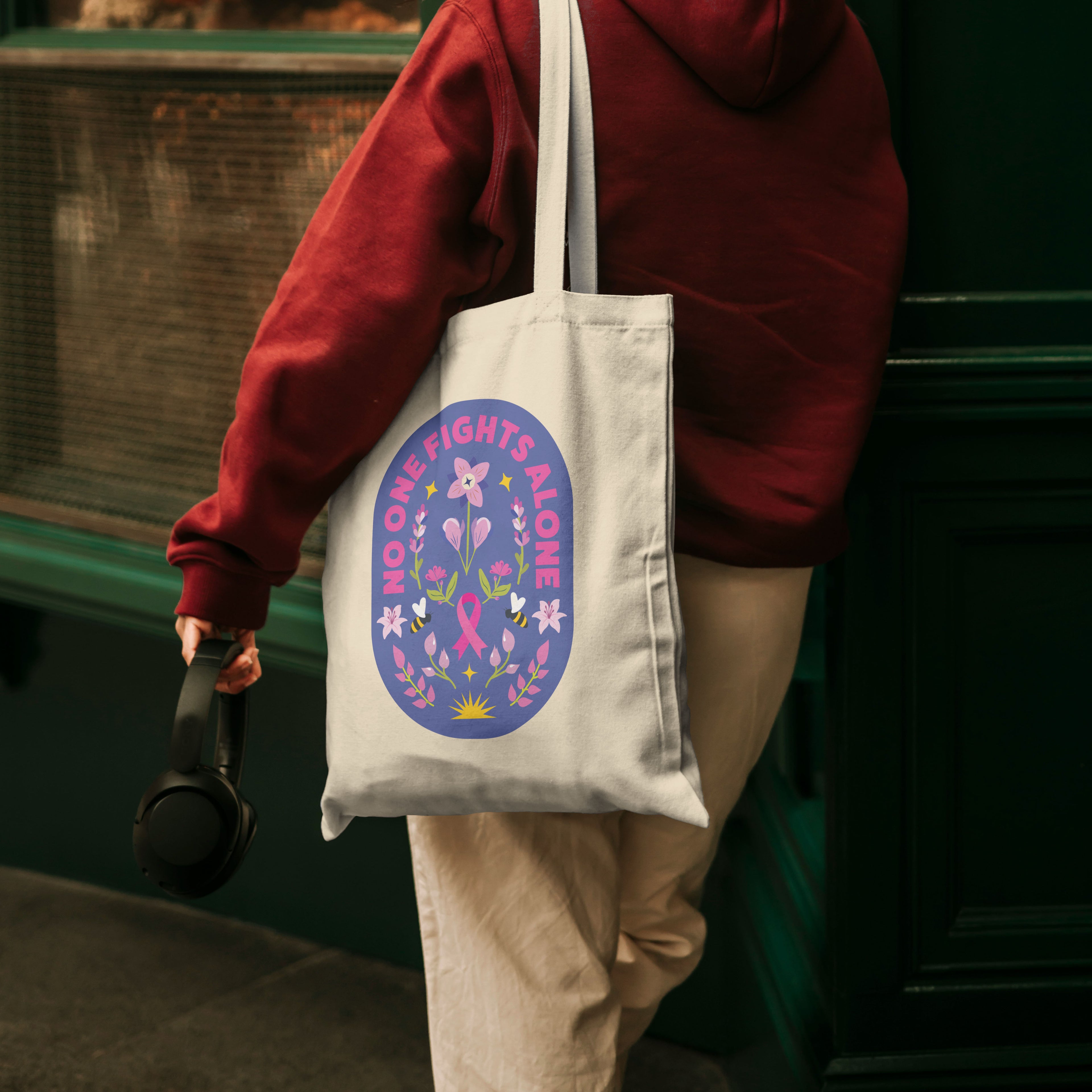 Person wearing a red hoodie holding a tote bag with a pink ribbon design.